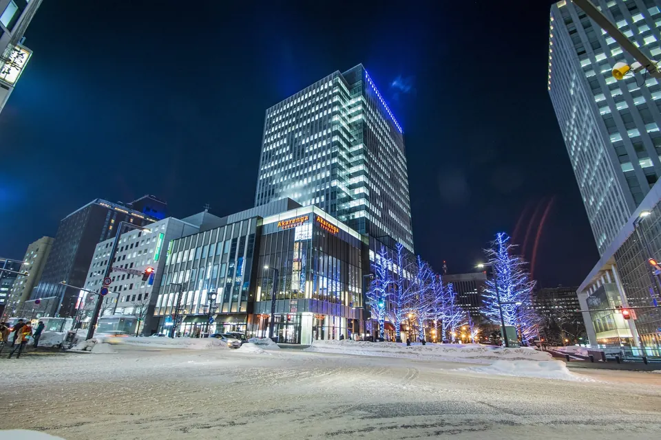 Illuminated buildings and a snowy intersection in front of Akarenga Terrace in Sapporo