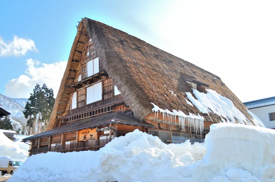 A steep thatched gassho-style roof rising above deep snow under a blue sky