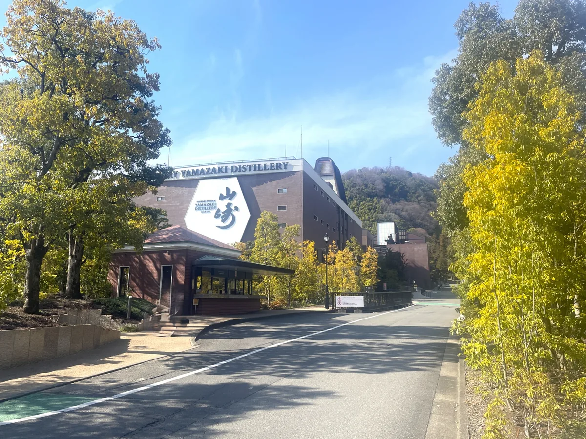 A tree-lined road beside Yamazaki Distillery, with its brick building and large Yamazaki sign